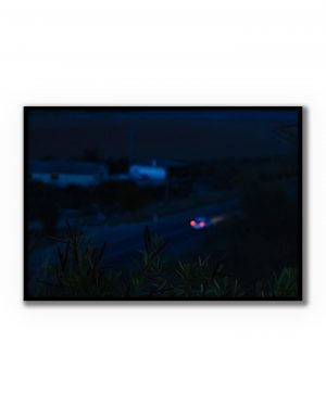 Fotografía nocturna de una carretera con un coche en movimiento y luces traseras rojas, escena minimalista y atmosférica.