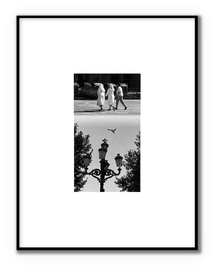 Fotografía urbana en blanco y negro con tres personas caminando y una farola clásica en composición vertical.